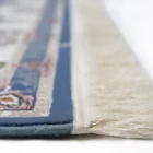 A close-up of a Qaleen Carpets rug's edge, featuring a blue and white border with a patterned design, with a focus on the