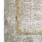 A close-up of a Qaleen Carpets rug with a gold border and intricate patterns, set against a white background