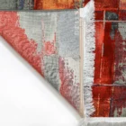 A close-up of a vibrant, hand-woven Qaleen Carpets rug with a unique, abstract design, featuring a mix of red, orange, and