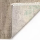 A close-up of a rug's corner, with a subtle pattern and a fringe of white, made by Qaleen Carpets