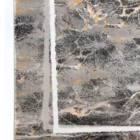A close-up of a Qaleen Carpets rug with a dark, marbled pattern and gold and white accents, set against a white background