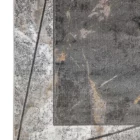 A close-up of a Qaleen Carpets rug with a mix of grey, white, and gold patterns, featuring a central grey rectangle with a