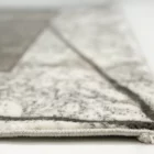 A close-up of a white and grey rug with a subtle, intricate pattern, made by Qaleen Carpets