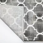Qaleen Carpets A close-up of a gray and white patterned rug with a corner folded up, showcasing its intricate design and