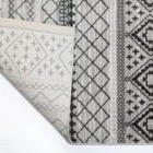 Qaleen Carpets A close-up of a rug's corner, with a pattern of geometric shapes and a neutral color palette