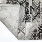 A close-up of a Qaleen Carpets rug with a white and black pattern, with a corner folded over to show the rug's edge and a