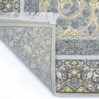 Qaleen Carpets A close-up of a gray and gold patterned rug with a fringe on the left side, against a white background