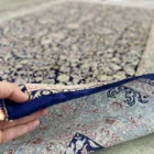 Carpets A person's hand holding the edge of a beautiful, intricately designed carpet, with a focus on the carpet's intricate