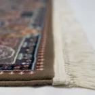 A close-up of a Qaleen Carpets rug with intricate patterns and a fringe of white, set against a white background