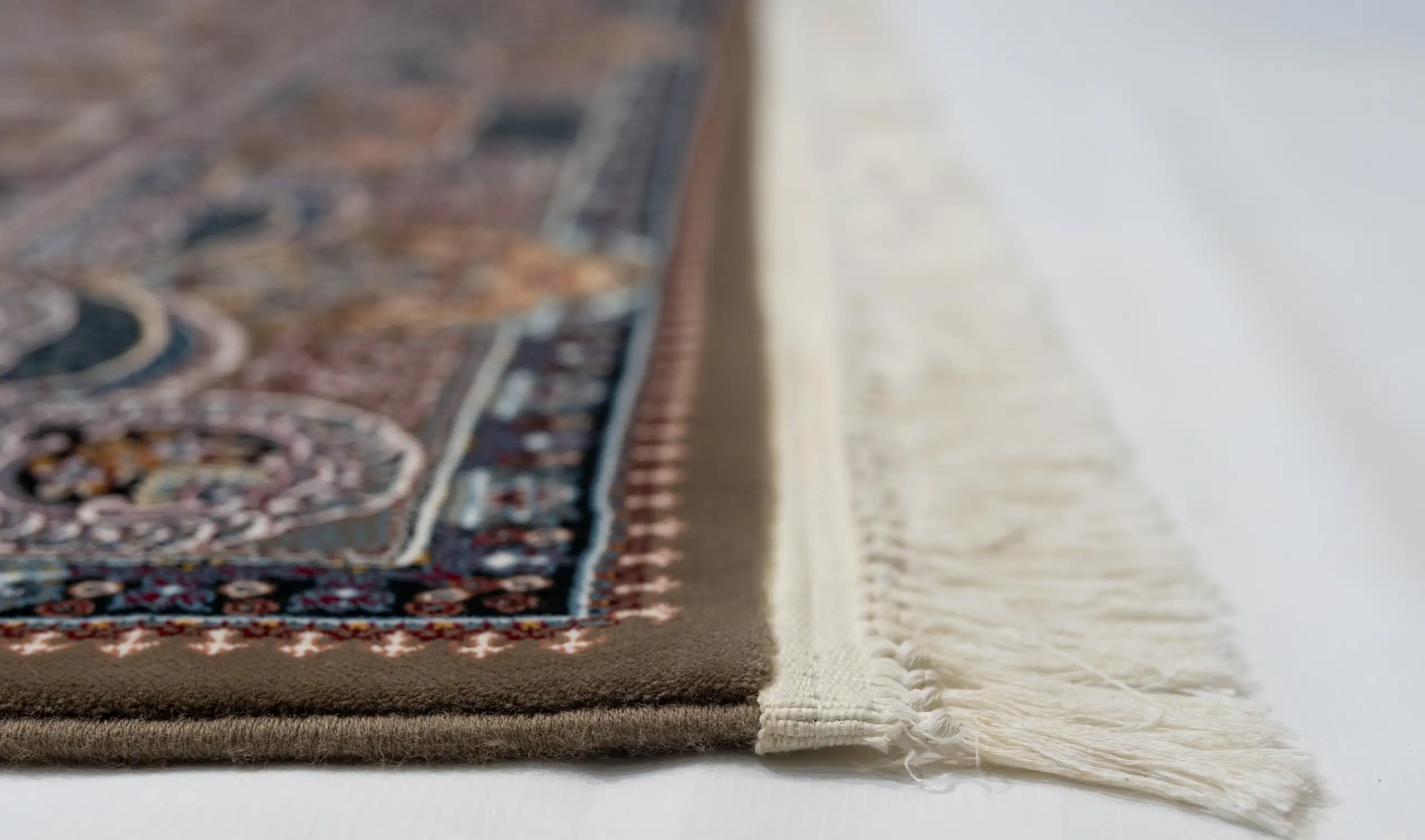 A close-up of a Qaleen Carpets rug with intricate patterns and a fringe of white, set against a white background
