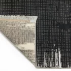 Qaleen Carpets A close-up view of a black and white rug with a fringe border, featuring a grid pattern and a corner turned