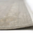 A close-up of a Qaleen Carpets rug with a soft, neutral color and subtle pattern, featuring a fringe on one edge