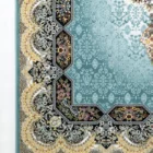 A close-up of a Qaleen Carpets rug with a blue and gold pattern, featuring a central hexagonal design and a border of