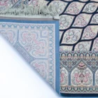 A Qaleen Carpets rug with a blue border and intricate patterns, partially unrolled to reveal its design and quality