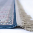 A close-up of a rug with a blue border and intricate patterns, made by Qaleen Carpets