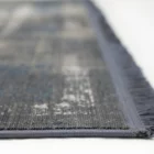 A close-up of a gray and blue rug with a fringe on one side, made by Qaleen Carpets
