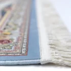 A close-up view of a rug with a blue border and intricate patterns, made by Qaleen Carpets