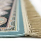 A close-up of a rug with a blue border and a patterned design, with a fringe at the bottom, made by Qaleen Carpets