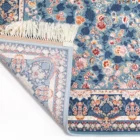 A Qaleen Carpets rug with a blue floral pattern and fringe, partially rolled up and against a white background